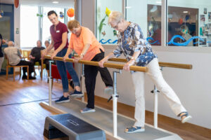 Eine Aktivierungsspezialistin zeigt zwei Frauen einfache Aerobic-Übungen am Barren in der Fitnessarena des Violino Zell.